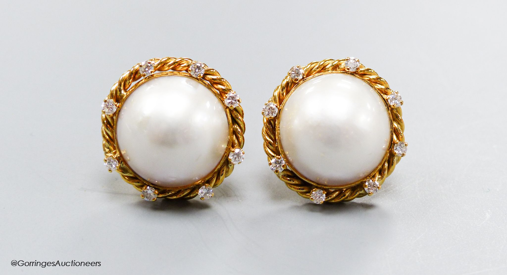 A modern pair of yellow metal (stamped 14k), mabe pearl set earrings, with diamond set rope twist border, 22mm
